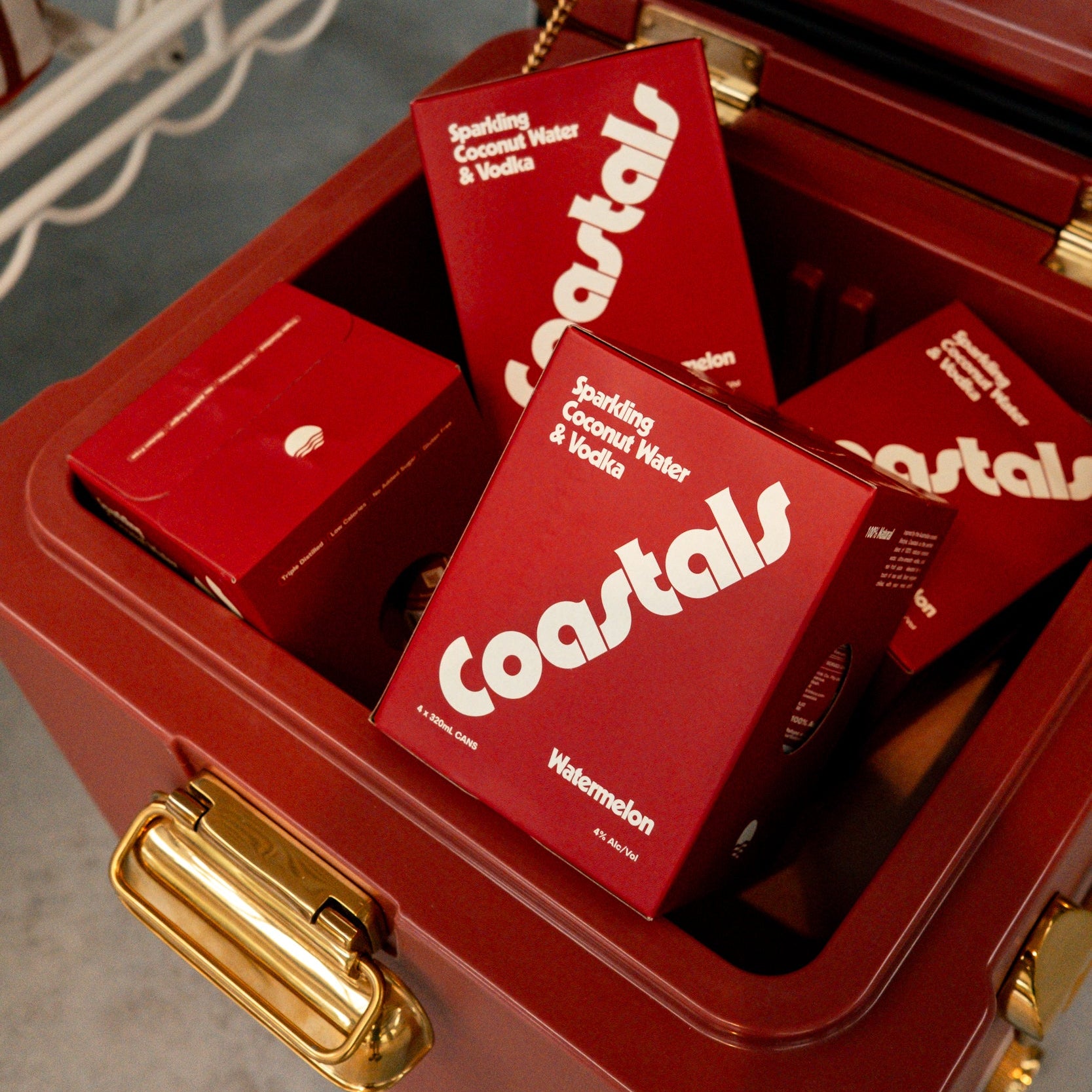 Red 'Coastals Watermelon' 4-pack boxes inside an open red esky with gold accents.
