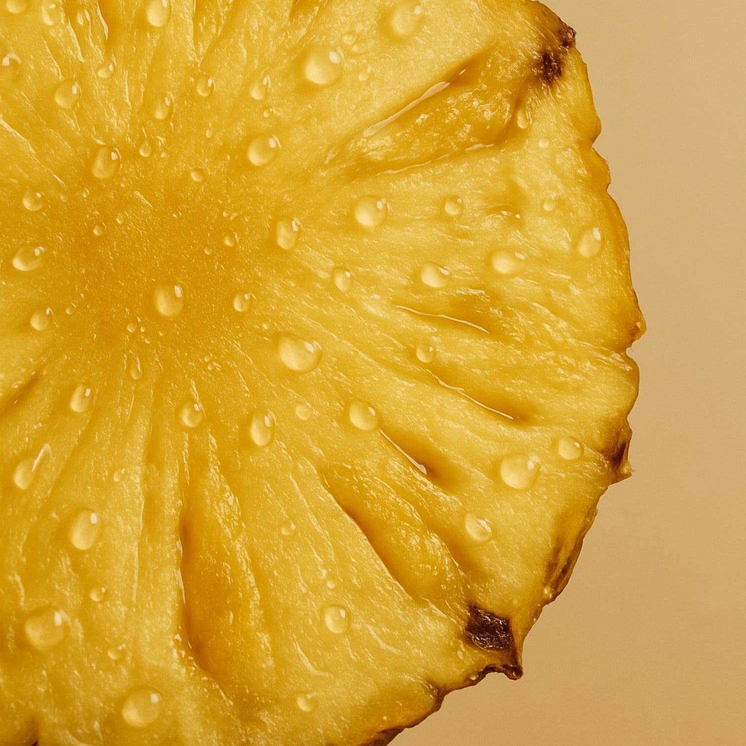 Close-up of a fresh pineapple slice with dewy droplets on a warm neutral background.