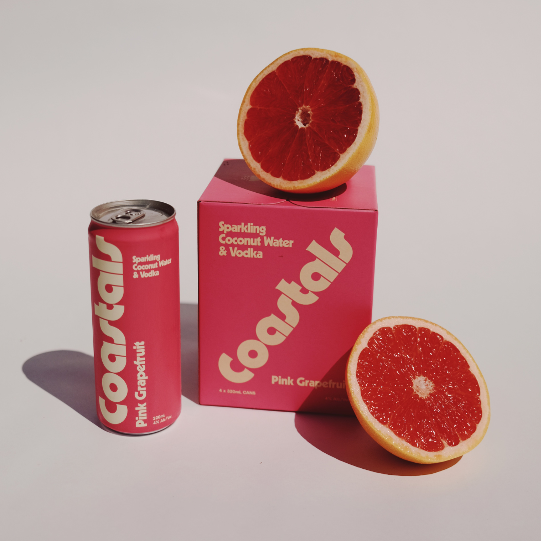 Coastals Pink Grapefruit sparkling coconut water and vodka, can and 4-pack with fresh grapefruit halves on a white background.